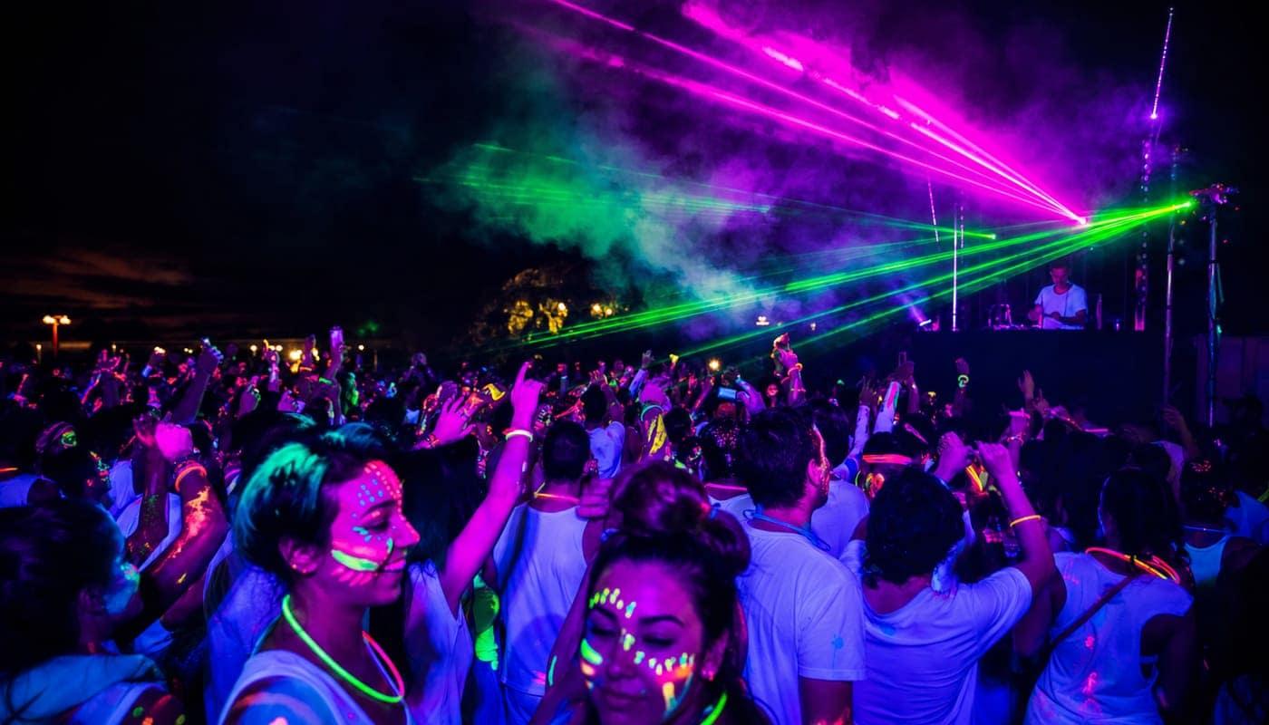 Multitud bailando con pintura fluor bajo luces UV y láseres en Festichola